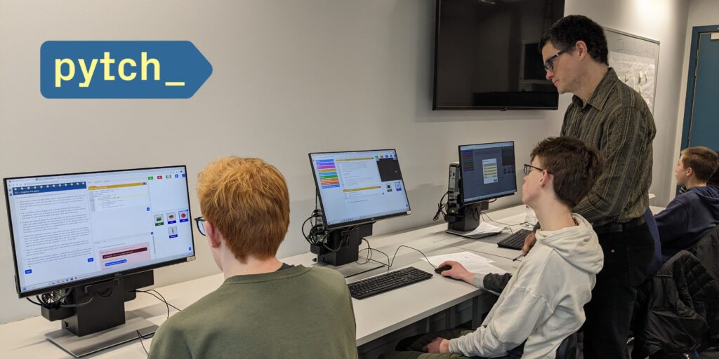 The picture shows Dr Ben North observing one students programming with the new script by script version of Pytch. Other two students are visible working on the same on their computers. The Pytch logo is visible on the top left hand corner.